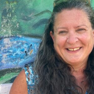 Kae Grant smiling at the camera while standing in front of a painted wall.