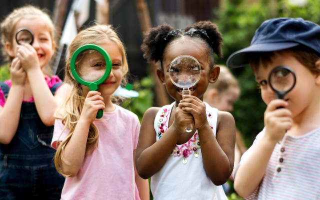 Four kids in a line looking at the camera through magnifying glasses.