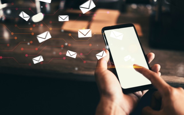 A phone being held with a finger touching the screen and little email icons coming from the phone.