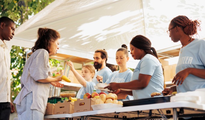 A line of people wearing blue shirts with "volunteer" on them handing out food to a line of people.
