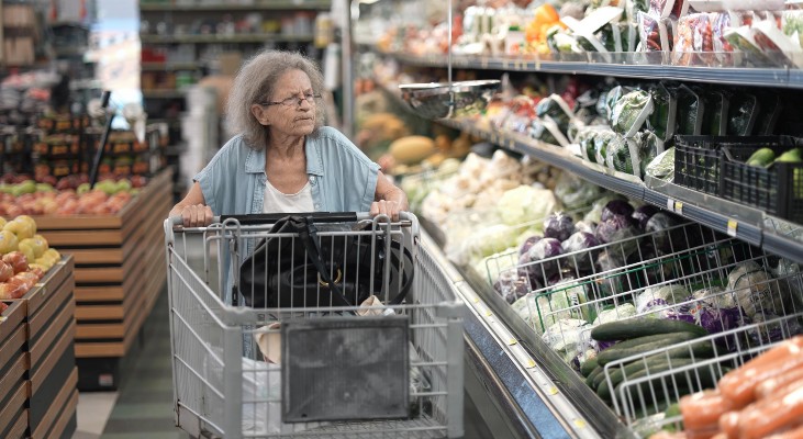 An older woman pushing a cart in a grocery store.