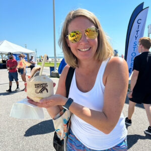 Kristin smiling at the camera with sunglasses on hodling a coconut with the phrase "Shrimpin' ain't easy" on it.